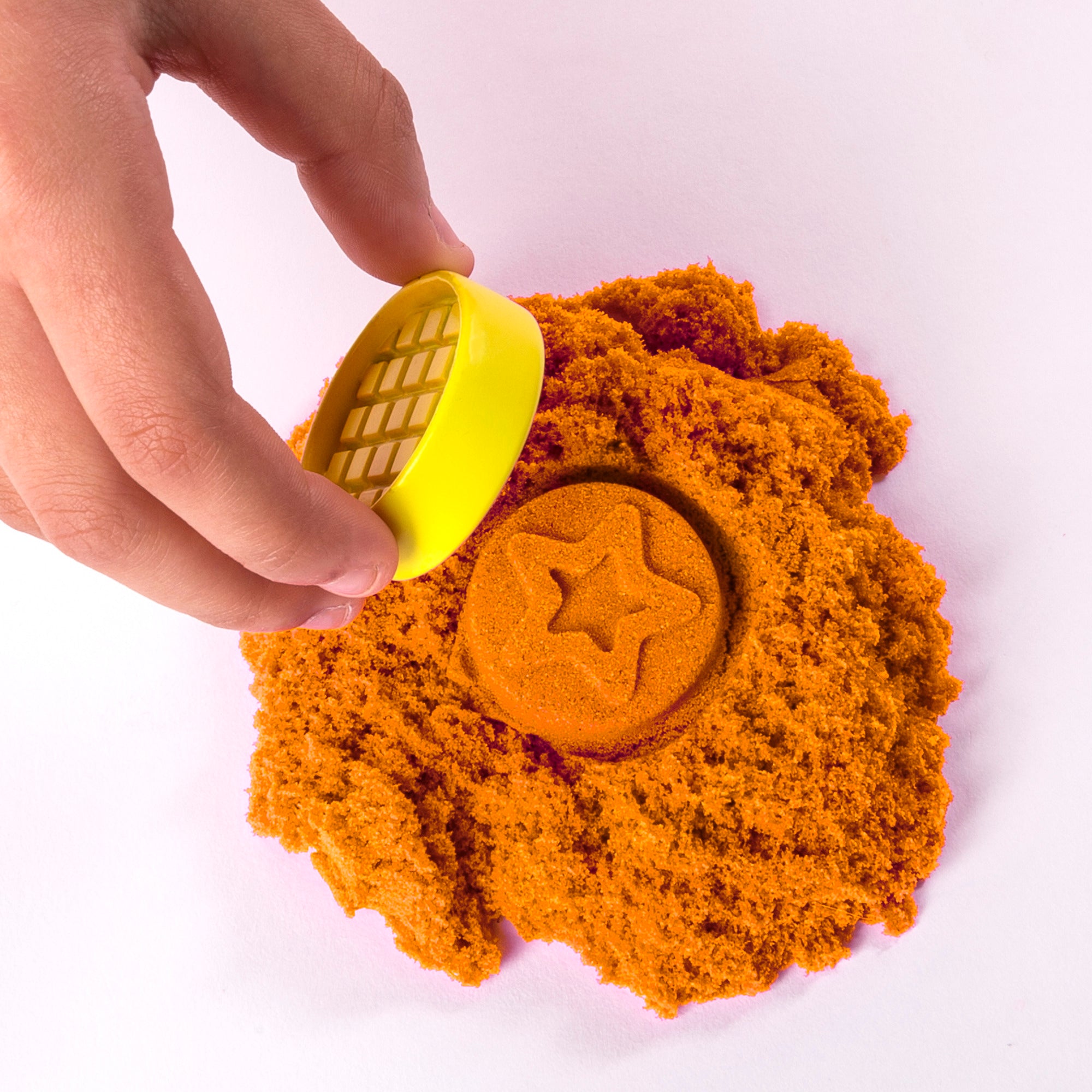 Barns hånd former magisk Kinetic Sand med gul udstikker til en orange stjerne.