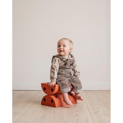 Baby sidder på to brændt orange Modu skamler på trægulv.