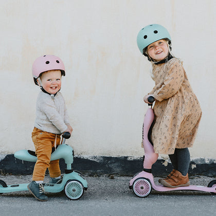 To piger med hjelme på Scoot and Ride løbehjul på fortovet.